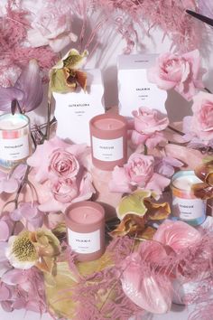 pink flowers and candles are arranged on a white surface with purple feathers around them, as well as cards