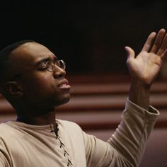 a man with his hands up in the air while wearing glasses and a beige sweater