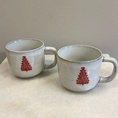 two white coffee cups with red christmas trees on them sitting on a marble counter top