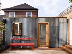 a red bench sitting on top of a wooden floor next to a metal wall and door