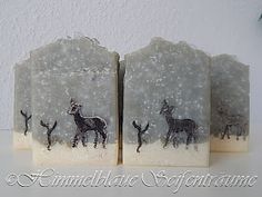 two soap blocks decorated with black and white deer on snow covered ground next to pine tree