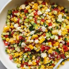 a white bowl filled with corn, cucumber and feta cheese