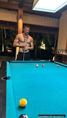 a shirtless man standing next to a pool table with balls on it and a cue in his hand