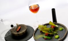 two plates with food on them next to a glass of wine and a teapot