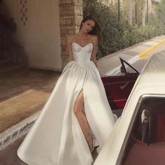 a woman standing next to a car wearing a white dress with high slits on the side