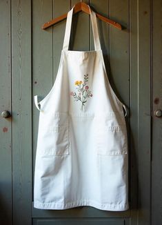 a white apron hanging on a wooden door with flowers embroidered on the front and back