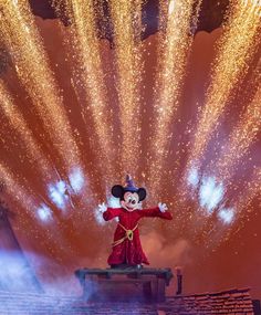 mickey mouse on top of a building with fireworks in the sky behind him and his arms outstretched