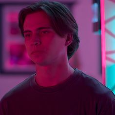 a young man standing in front of a wall with pink light on it's face