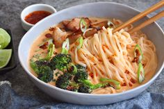 a bowl filled with noodles, broccoli and meat next to some dipping sauce