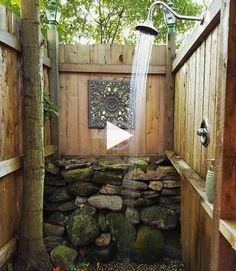 an outdoor shower with rocks and water coming from the faucet, in front of a wooden fence