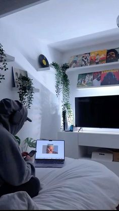 a person sitting on a bed with a laptop in front of them and a television behind them