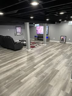 an empty room with grey walls and wooden floors, two black recliners in the middle