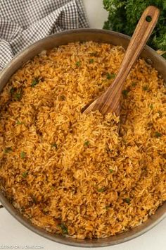 a pan filled with rice and parsley on top of a counter next to a wooden spoon