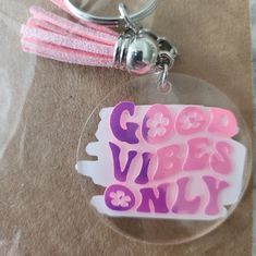 a plastic keychain with the words good viber only on it and a pink ribbon