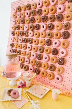 a table topped with lots of donuts on top of a pink and yellow wall