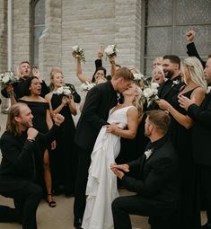 a bride and groom kissing in front of a group of wedding party members holding bouquets