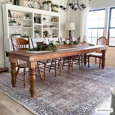 a dining room table with chairs and an area rug in front of the table is decorated with greenery