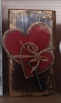 a red heart is tied up to a wooden block with a key in it on a shelf