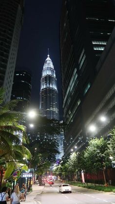 a city street with tall buildings and cars driving down the road in front of it at night