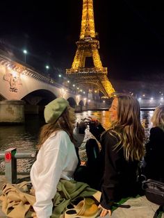 two women sitting on the ground in front of the eiffel tower at night