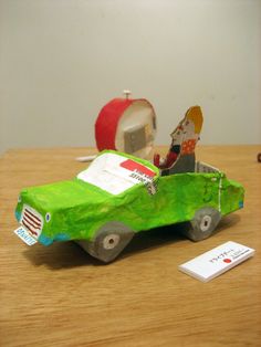 a toy car with an apple in the back sitting on a table next to a piece of paper