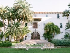 an outdoor ceremony setup with white chairs and palm trees in front of a large building