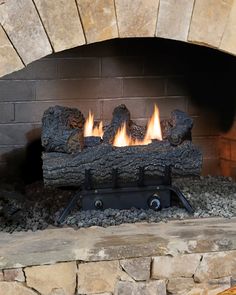 a fire is burning in a fireplace with rocks on the sides and logs around it