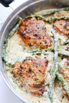 a pan filled with chicken and asparagus covered in cream sauce on top of a table