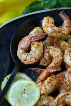 a black plate topped with shrimp and lemon wedges