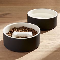 two black and white bowls filled with food on top of a wooden table