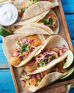 fish tacos with coleslaw and slaw are served on a wooden tray