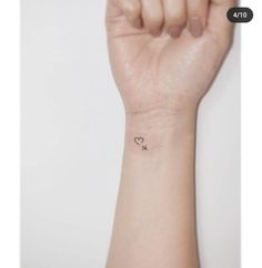 a small wrist tattoo with a heart and arrow on the left side of the arm