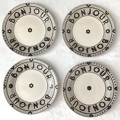 four black and white plates with the words bonjou on each one, in different languages