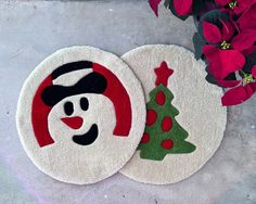 two christmas tree and snowman rugs sitting next to red flowers