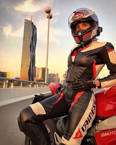 a woman in black and red leather outfit sitting on a motorbike with cityscape in the background