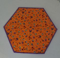 an orange and purple hexagonal table cloth with various designs on it, sitting on a white surface