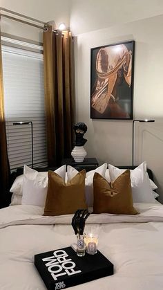 a white bed topped with lots of pillows next to a painting on the wall above it