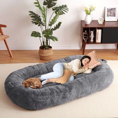 a woman laying on top of a dog bed with a large pillow and pillows in front of her