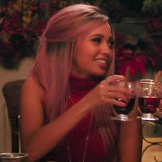 a woman sitting at a table with two wine glasses in front of her and smiling