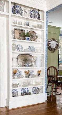 a white bookcase with blue and white china on it in a living room next to a dining room table