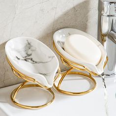 two white and gold dishes sitting on top of a sink next to a faucet