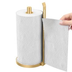 a hand holding a roll of toilet paper in front of a gold holder on a white background