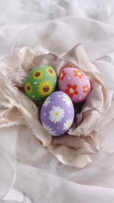 four painted eggs in a paper bag on a white cloth covered tablecloth, with sunflowers and daisies