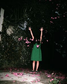 a woman in a green dress throwing pink flowers into the air with her arms up