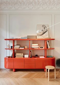 an orange shelf with books and magazines on it in a white walled living room area