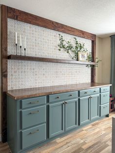 a kitchen with blue cabinets and wooden shelves on the wall next to a potted plant