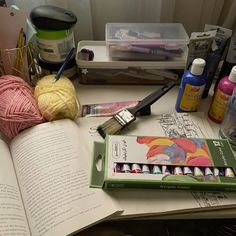 an open book sitting on top of a table next to yarn and crochet hooks