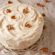 a white frosted cake with walnuts on top sitting on a glass platter