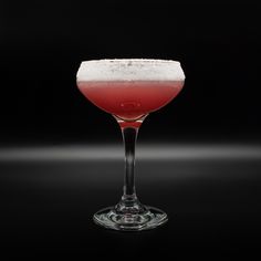 a red drink in a wine glass on a black background with the light reflecting off it's rim