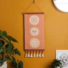 a wall hanging with two sun and moon designs on it next to a potted plant